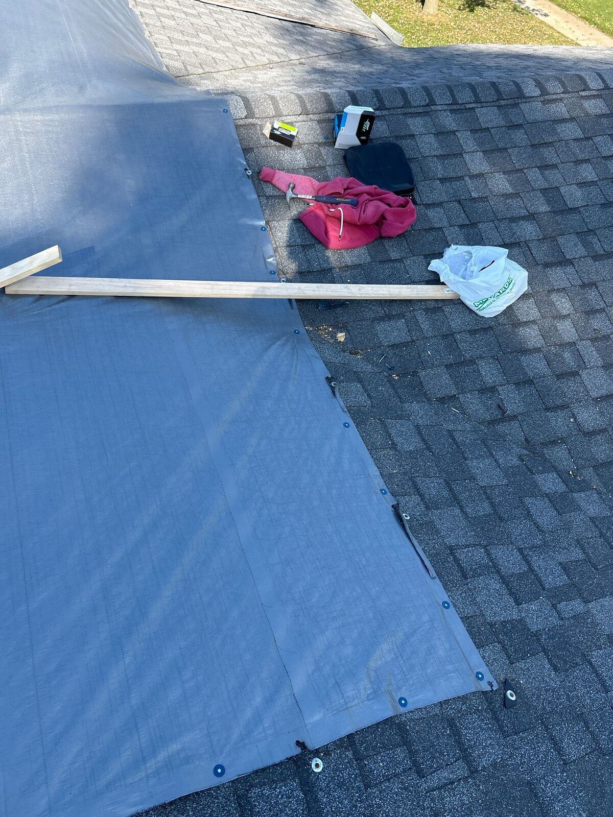 Edge of an emergency roof tarp secured with wood battens on a shingle roof