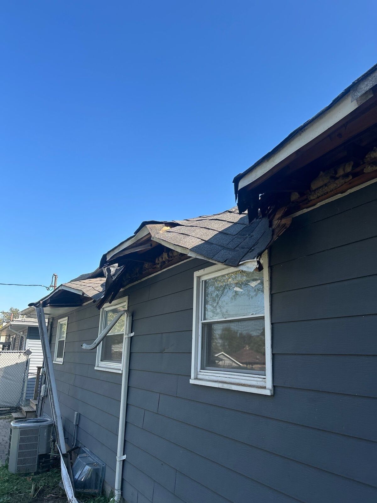 Wind-torn roof edge with shingles and soffit ripped away above a window