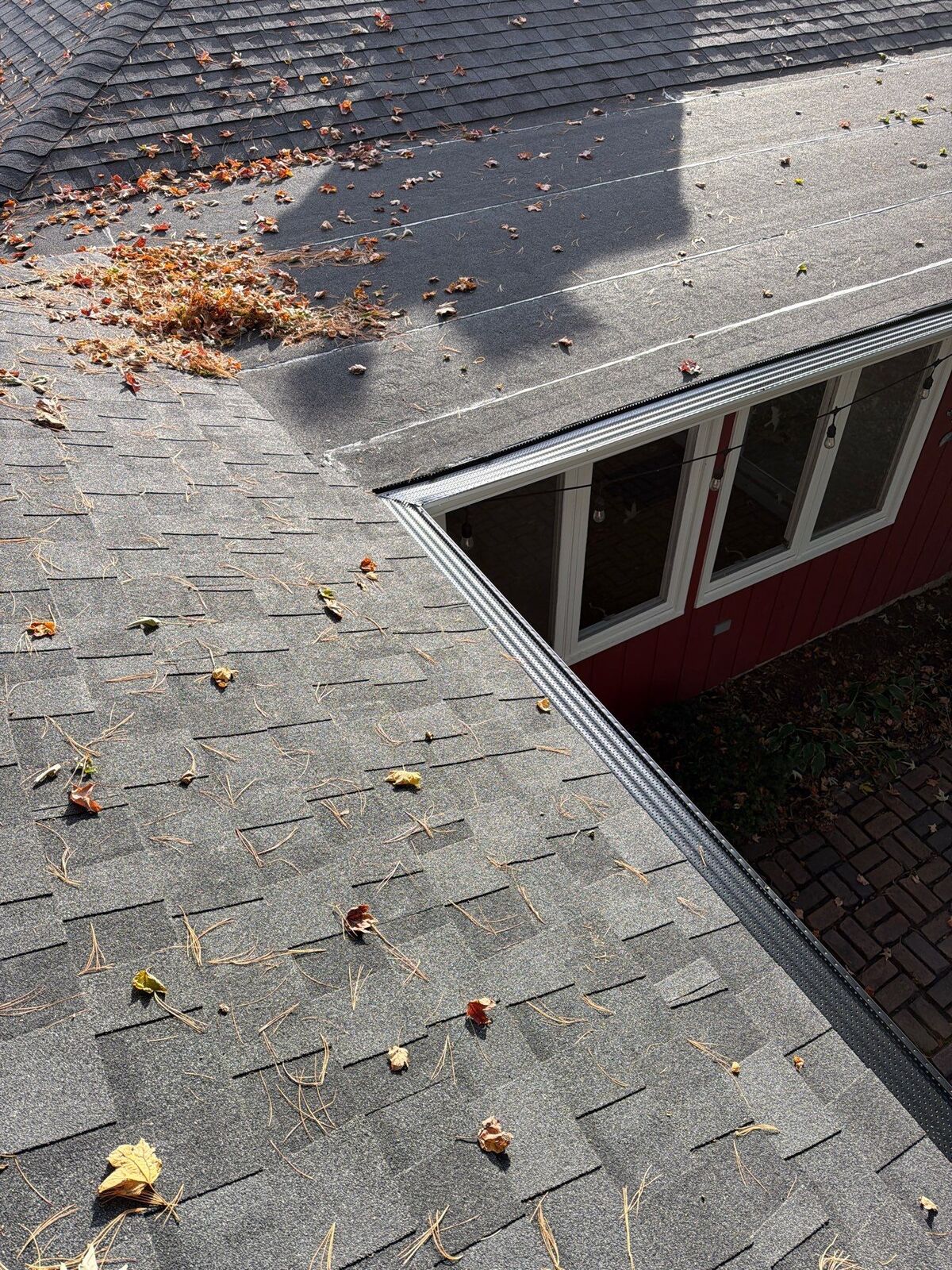Roof valley covered in wind-blown leaves and debris above a window